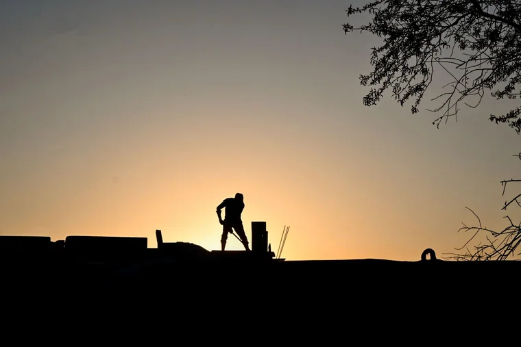 A roofer working on a roofline against an early morning sky